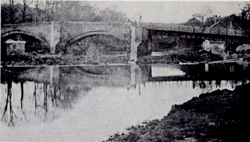 Old stone Sheepwash Bridge ruin with wooden footbridge alongside